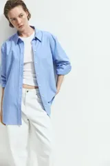 Camisa de algodón color celeste, con cuello clásico, cierre frontal de botones y mangas largas con puños sencillos. Presenta corte relajado y bajo redondeado.