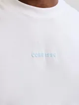 Musculosa blanca de algodón con cuello redondo, calce holgado y estampa gráfica pequeña en el frente.