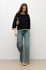 Sweater de punto negro con escote bote, mangas largas y detalles de terminación en ondas de color blanco en el cuello, los puños y el ruedo.