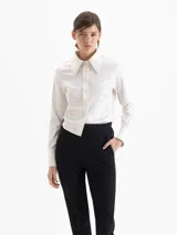 Camisa de jacquard con diseño floral sutil, color blanco, de corte regular y largo a la cadera. Presenta cuello amplio con puntas marcadas, cierre frontal con botones y mangas largas con puños estructurados.