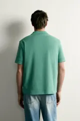 Remera polo regular fit de color gris oscuro, confeccionada en tejido de algodón con textura de rayas verticales. Cuenta con cuello solapa, cierre frontal con botones y mangas cortas con terminación en rib.