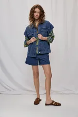 Chaleco oversize de jean negro, con cuello camisero, cierre frontal con botones metálicos y bolsillos delanteros.