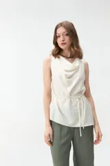 Musculosa sin mangas de color blanco, con cuello drapeado y lazo fino para ajustar en la cintura.