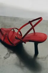 Sandalia de piel color rojo con diseño de tiras finas en la parte delantera. Cuenta con cierre de pulsera al tobillo mediante hebilla metálica y tacón de altura media en color negro.