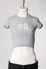 Baby tee de calce al cuerpo y manga corta, con cuello redondo y diseño con tachas frontales.