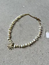 Gargantilla artesanal compuesta por piedras naturales blancas irregulares intercaladas con pequeñas cuentas doradas. Presenta un dije central en forma de sol de bronce y cuenta con cadena de alargue con cierre de mosquetón.