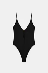 Body negro de escote en V profundo y tirantes finos. Detalle de abertura en delantero con aplique metálico dorado. Cierre en la parte inferior con botones a presión.