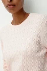 Buzo entallado color rosado claro, de punto trenzado, con cuello redondo y un pequeño corazón bordado en el pecho. Presenta ribete acanalado en cuello, puños y bajo.