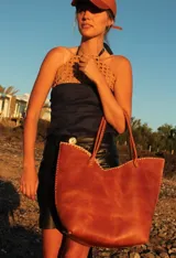 Cartera de cuero color marrón chocolate con manijas largas y borde superior en corte en V. Diseño amplio y liviano, con terminaciones artesanales y costuras contrastantes en todo el contorno.