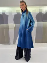 Tapado largo de fieltro de lana merino con teñido artesanal tie-dye en degradé de celeste a azul. Tiene cuello alto, cierre lateral con broches ocultos, bolsillos laterales y corte amplio.