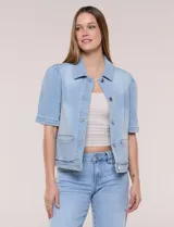 Camperita de denim color celeste con efecto lavado suave, cuello camisero clásico y cierre frontal de botones metálicos. Tiene mangas cortas con fruncido en los hombros, bolsillos delanteros bajos y costuras estructuradas.