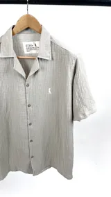 Camisa de manga corta color verde seco, confeccionada en muselina con cuello cubano y cierre frontal con botones.