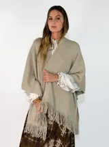 Ruana de tejido de punto en color beige con acabado brillante y flecos en los extremos.