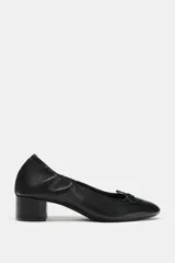 Zapato tipo bailarina de piel color negro, con tacón bloque bajo, puntera redonda y detalle de pequeño lazo en la parte delantera.