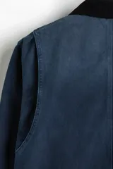 Campera worker corta de sarga de algodón en color azul oscuro, con cuello de pana negro en contraste. Cuenta con cierre frontal oculto por solapa con botones a presión y grandes bolsillos frontales tipo parche.