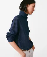 Blusa de cuello alto con diseño de rayas verticales finas, confeccionada en una mezcla de viscosa, poliamida y poliéster. Presenta cierre frontal de botones y mangas largas con puños abotonados.