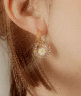 Aros colgantes con forma circular, con strass plateado alrededor y flor de vidrio amarilla con centro rojo en el interior. El arito es de acero quirúrgico.