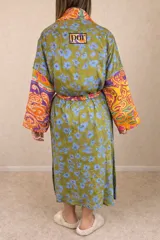 Bata tipo kimono de diseño patchwork, confeccionada con una mezcla de telas estampadas con motivos florales, paisley y geométricos en tonos verdes, naranjas y violetas. Presenta mangas tres cuartos, aberturas laterales en el ruedo y un lazo ajustable en la cintura.
