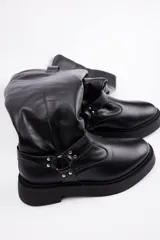 Bota de caña alta confeccionada en cuero vacuno color negro, con suela track de plataforma y detalle de tira con argolla metálica y tachas en el tobillo.