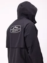 Campera impermeable Rusty con capucha, confeccionada en nylon. Presenta cierre frontal con botones a presión, bolsillos delanteros con solapa y puños elásticos.