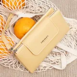 Billetera larga color beige, con textura granulada, solapa frontal con cierre magnético y logo de la marca grabado. Incluye correa de mano extraíble y compartimento principal con cierre.