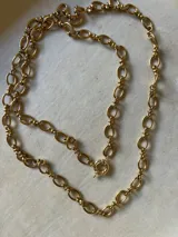 Collar largo tipo cadena con eslabones ovalados alargados unidos por eslabones circulares pequeños. Presenta un cierre tipo sailor clasp circular y cuenta con un acabado dorado brillante.