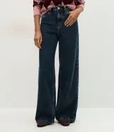 Pantalón wide leg de tiro alto en denim azul oscuro, con trabillas para cinturón, cierre de botón y cremallera, y bolsillos delanteros y traseros.