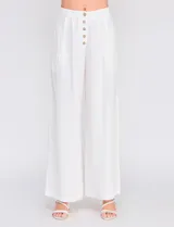 Pantalón palazzo color blanco, confeccionado en mezcla de lino y viscosa, de tiro alto con cierre frontal de botones, pinzas en la cintura y piernas anchas.