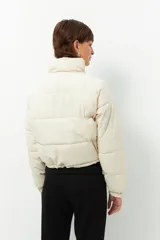 Campera puffer corta color beige de nylon, con cuello alto, cierre frontal y bolsillos laterales con cierre.