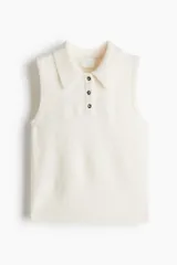 Chaleco corto de punto suave color blanco hueso, con cuello camisero y tapeta de tres botones oscuros. Presenta ribete acanalado en sisas y bajo.