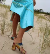 Sandalias de tacón alto con diseño de dos tiras anchas, confeccionadas en tela con estampado abstracto en tonos dorados y negros. Presentan un tacón cuadrado forrado en el mismo tejido.