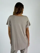 Blusa de satén color blanco, con cuello en V, mangas cortas y corte holgado con dobladillo asimétrico más largo en la parte posterior.