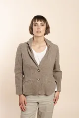 Chaqueta de corte recto color marrón claro, confeccionada en lana fina sin teñir. Tiene cuello con solapa, bolsillos ojal, forro en las mangas y terminaciones envivadas. Es más larga en la espalda que en la delantera y se abrocha con dos botones.