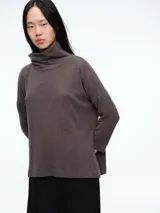 Buzo tejido de punto en color marrón, con cuello alto tipo polera, sisa caída y tajos laterales en el ruedo.