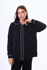 Camisa negra de manga larga con cuello estilo pijama y cierre frontal de botones. Presenta un vivo blanco en contraste que recorre el cuello, la tapeta de botones y los puños.