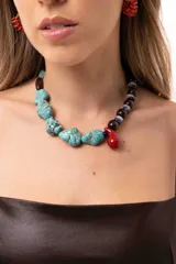 Collar de diseño irregular compuesto por una mitad de cuentas de piedra turquesa y la otra mitad de cuentas de madera, piedras naturales y acrílico, con un dije central en forma de gota roja.