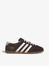 Championes Adidas Gazelle Lo Pro, modelo de corte bajo confeccionado en gamuza marrón con las tres tiras características en blanco, cordones blancos y suela de goma translúcida.