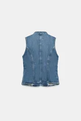 Top de denim blanco sin mangas, con cuello mao y cierre frontal cruzado con trabillas y botones metálicos.