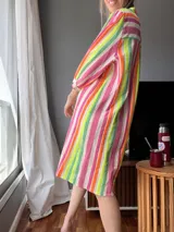 Vestido camisero largo con estampado de rayas verticales en tonos rosa, naranja, verde y blanco. Tiene cuello mao, mangas 3/4 con puños y cierre frontal con botones.