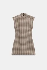 Mono corto de cuello subido y manga sisa con hombreras, con diseño de cuadros tipo tartán en tonos beige y negro. Cuenta con trabillas en los hombros y cierre en la espalda con cremallera oculta.