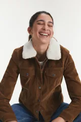 Campera tipo trucker de gamuza sintética color marrón, con cuello de corderito blanco, cierre frontal con botones metálicos y bolsillos en el pecho.