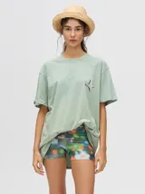 Remera verde agua con cuello redondo y manga corta, con un pequeño estampado de una estrella en el pecho. Corte holgado y cuadrado.