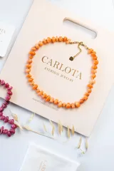 Gargantilla de acero quirúrgico con baño de oro, con cuentas de piedra natural naranjas y esferas doradas.