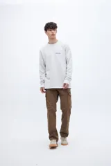 Buzo gris de felpa liviana con cuello redondo, mangas largas y puños ajustados. Tiene un bordado pequeño en el pecho y un diseño estampado en la espalda.