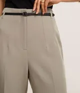 Pantalón de sastrería corte carrot, color beige, con cintura alta, pinzas frontales y cinturón fino incorporado con hebilla metálica.