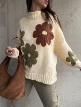 Sweater de tejido de punto color natural, con diseño de flores grandes aplicadas en tonos marrón y verde oliva. Presenta cuello redondo, mangas largas y corte holgado.