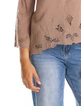 Blusa de rayón color marrón con escote en V y mangas tres cuartos acampanadas. Presenta detalles de bordado suizo y calados florales en los puños y en el ruedo asimétrico con terminación festoneada.