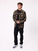 Camisa de manga larga confeccionada en franela de algodón, con diseño de cuadros en tonos verde y marrón. Presenta cuello clásico, cierre frontal con botones y dos bolsillos en el pecho con solapa.