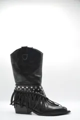 Bota de cuero negro estilo texano, con taco bajo y punta fina. Incluye un aplique desmontable en la zona del empeine decorado con tachas metálicas y flecos largos.