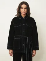 Chaqueta de terciopelo en color azul oscuro, con corte recto, cuello camisero, cierre frontal con botones metálicos y costuras a la vista en contraste. Presenta bolsillos frontales tipo parche.